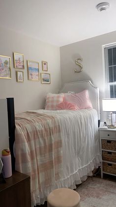 a bedroom with pink and white bedding, pictures on the wall and a window