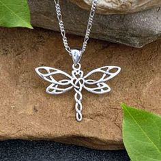 a silver dragon pendant sitting on top of a rock next to a leafy plant