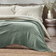 a bed with green sheets and pillows in a room next to two white vases