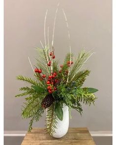 a white vase filled with red berries and greenery on top of a wooden table