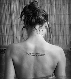 a woman with a tattoo on her back sitting in a bathtub and looking at the water