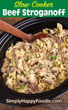 slow cooker beef stroganonoff in a black crock pot with a wooden spoon