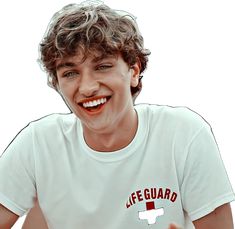 a young man with curly hair wearing a lifeguard t - shirt and pointing at the camera