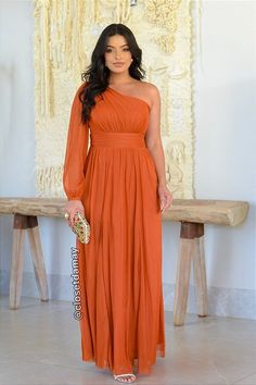 a woman in an orange dress standing next to a bench and holding a white purse