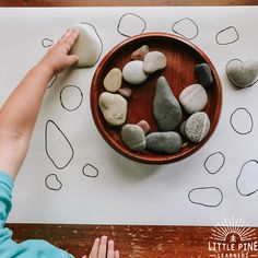 a child is playing with rocks in a wooden bowl on top of a paper sheet