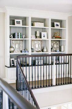 a staircase leading to a white bookcase with black railings and shelves on either side