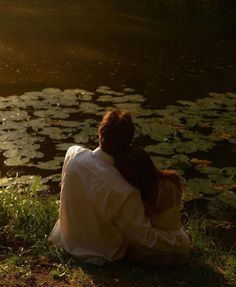 a woman sitting on the ground next to a body of water with lily pads in it