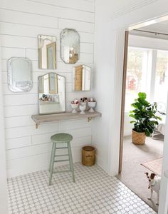 a bathroom with white walls and tile flooring, mirrors on the wall and stool