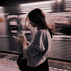 a woman standing in front of a train while looking at her cell phone and reading