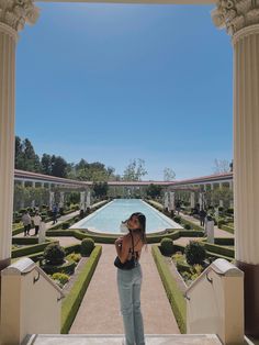 a woman standing in front of a pool surrounded by trees and bushes, taking a photo