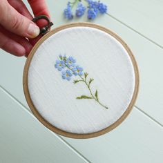 a hand holding a small embroidery kit with blue flowers