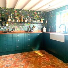 a kitchen with green cabinets and floral wallpaper on the walls, along with an orange tiled floor