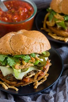 two black plates topped with sandwiches next to a bowl of salsa and chips on a table