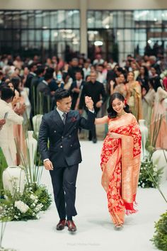 a man and woman walking down a runway with people in the background holding their hands up