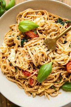 a white bowl filled with pasta and spinach on top of a wooden table next to a fork