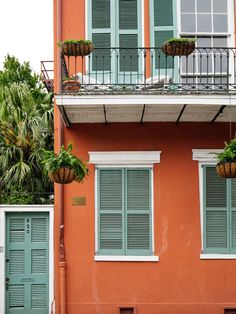 an orange building with blue shutters and green plants on the balconies above