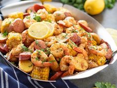 shrimp and corn on the cob in a bowl with lemon wedges next to it