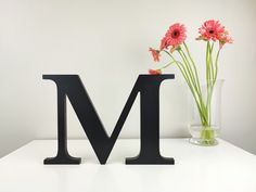 the letter m is next to a vase with flowers in it on a white surface