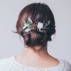 a woman with a flower in her hair wearing a white top and red berries on the back of her head