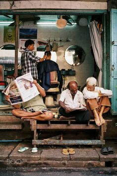 three men sitting on a bench in front of a store with their feet propped up