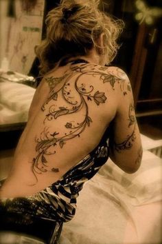 a woman sitting on top of a bed with tattoos on her back and arms behind her head