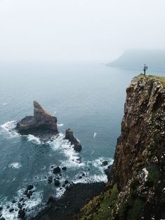 a person standing on top of a cliff next to the ocean