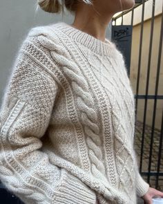 a woman wearing a white sweater and black pants is standing in front of a fence