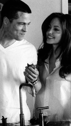 a man and woman standing next to each other in front of a sink with faucets