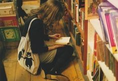 a woman sitting on the floor in front of bookshelves and looking at her book