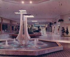 a fountain in the middle of a mall with lights shining on it's sides