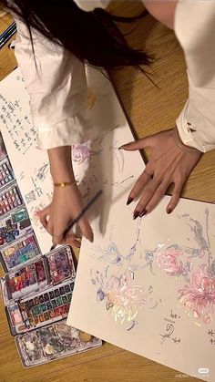 a woman is painting flowers with watercolors on paper