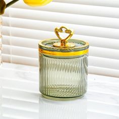 a glass jar with a gold heart on top sitting next to a yellow tulip