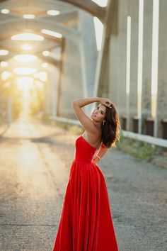 a woman in a red dress standing on the side of a road with her arms behind her head