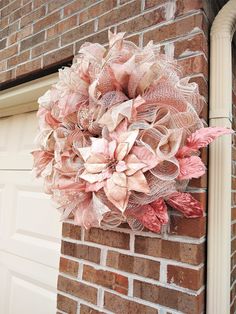 a wreath is hanging on the side of a brick building with flowers in pink and white