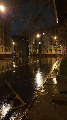 an empty street at night with rain on the ground and buildings in the backround