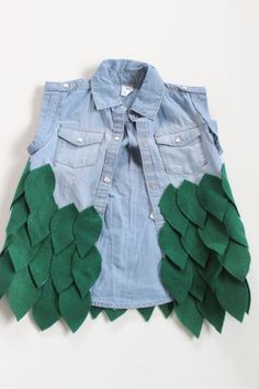 a denim jacket with green leaves on the front and back, sitting on top of a white surface