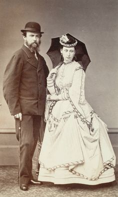 an old black and white photo of a man and woman dressed in period clothing, standing under an umbrella