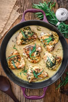 chicken with cream sauce and herbs in a skillet on a wooden table next to a sprig of rosemary