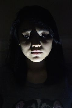 a woman with black hair and eyes is looking at her cell phone in the dark