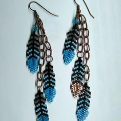 two pairs of blue and black beaded earrings hanging from copper hooks on a white surface