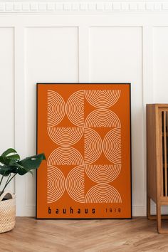 an orange poster sitting on top of a wooden floor next to a potted plant