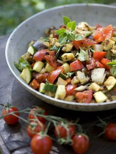 a salad in a bowl with tomatoes, cucumbers and herbs on the side