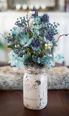 a mason jar filled with blue flowers on top of a wooden table next to a window