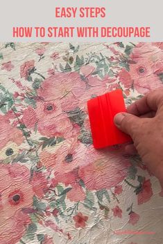 someone is using a red sponge to clean the fabric on a floral print tablecloth