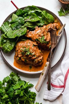 two meatballs covered in sauce and spinach leaves on a plate with a fork