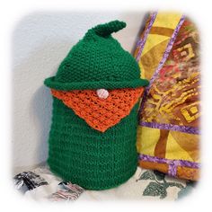 a crocheted green bag with an orange nose and hat on it sitting next to a pillow