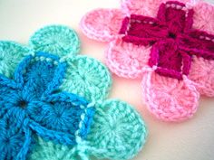 three crocheted flowers sitting on top of a white table next to each other