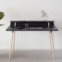 a black desk with two wooden legs and a laptop on it, next to a potted plant