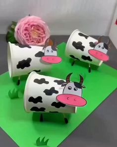 three paper cows with flowers in them on top of green mating and pink flower