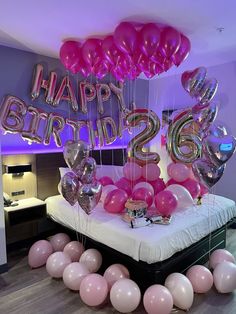 a bed topped with lots of pink and silver balloons next to a wall that says happy birthday